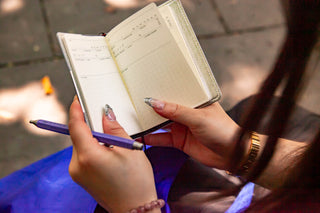 Hands writing in an open pocket log diary refill, with a purple pen and lined page