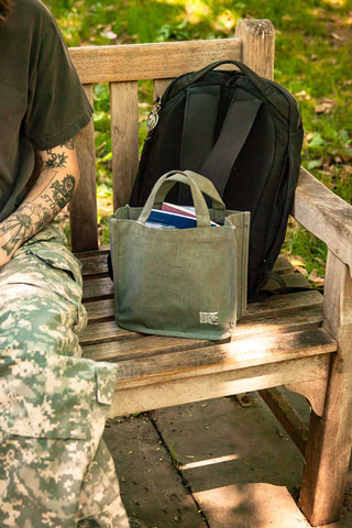 Olive canvas tool tote with short handles, standing on a bench outdoors