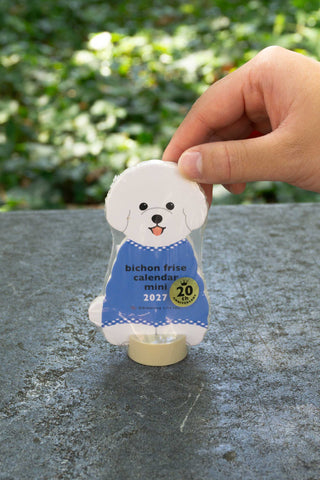 Mini die-cut Bichon Frise calendar stand held by hand, blue 2027 badge