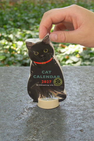 Cat die-cut calendar with black cat cutout held by hand above clear base stand
