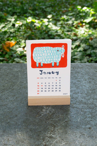 January 2027 stand calendar with blue patterned sheep illustration on white card, wooden base
