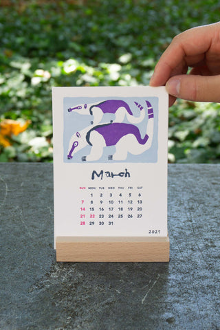 March 2027 stand calendar with purple and gray animal illustration on white card, wooden base