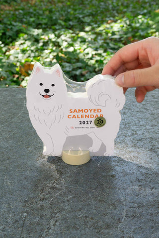 Samoyed die-cut calendar stand being lifted by hand, showing 2027 and seal