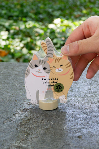 Twin cats mini die-cut calendar held by hand, cream and orange cat figures