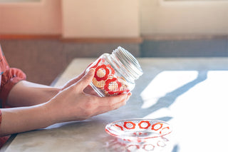 Mini candy jar held in hand, clear glass with red circular pattern and silver lid