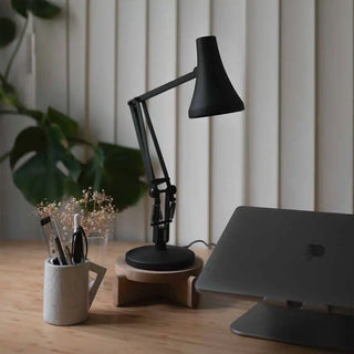 Carbon black mini desk lamp with conical shade on a wooden desk, adjustable arm