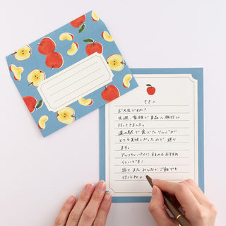 Fruit illustrated letter card with lined writing area and apple motif, held with pen and hands