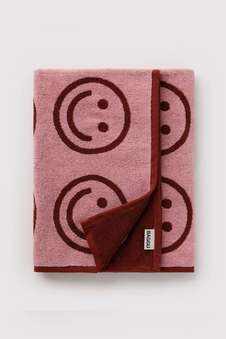 Blush pink bath towel folded over with brown smiley print and small label