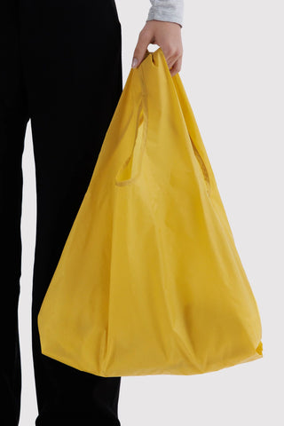 Yellow tote bag held in hand with gathered bottom and blue logo patch