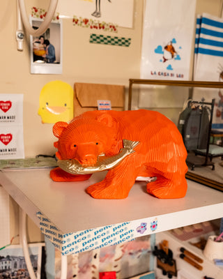 Orange carved wooden bear coin bank with coin slot on back, front view on shelf