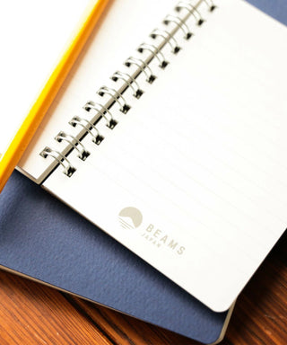 Navy notebook with open lined pages and spiral rings visible; BEAMS Japan logo on page.