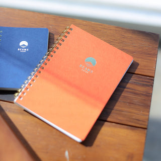 Orange lined notebook with spiral binding and BEAMS Japan logo on cover.