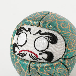 Embroidered Daruma-style face patch on teal patterned fabric with swirls