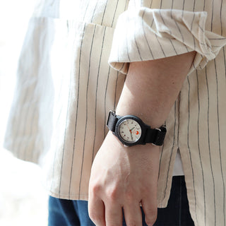 Black wristwatch on wrist against striped shirt sleeve and dark pants