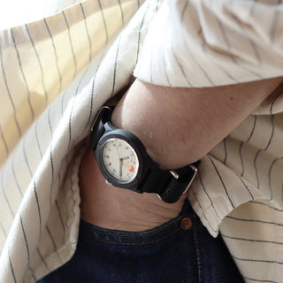 Black wristwatch on wrist with black dial and strap, worn with striped button-down shirt