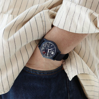 Navy round wrist watch on fabric strap worn on arm; dark dial with numeric markers