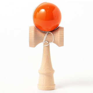 Wooden kendama with orange ball perched on top cup, white cord tied around