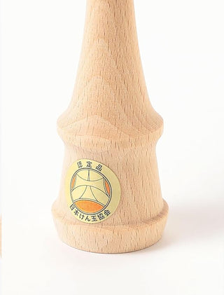 Wooden kendama base with circular logo patch on natural wood, orange ball on top