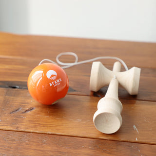 Wooden kendama on wooden table: orange ball, cups, and white handle pieces with cord