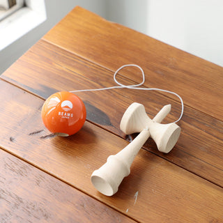 Wooden kendama on wooden table with orange ball and white cord, natural wood cups