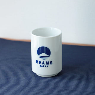 White sushi cup with blue BEAMS Japan logo on front, on dark cloth.