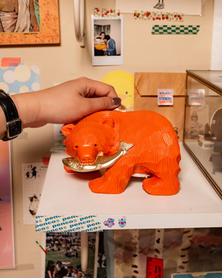 Orange carved wooden bear coin bank held by hand, coin tray visible