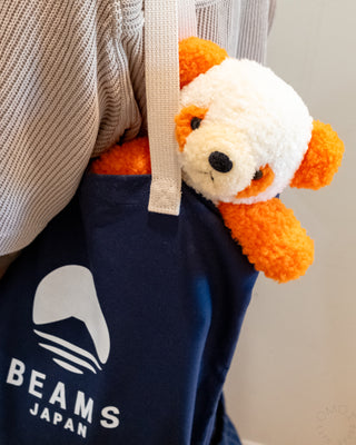 Orange-and-white plush panda attached to navy BEAMS Japan tote bag, side view