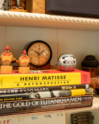 Teal Daruma-style ornament on a shelf with embroidered face and red details