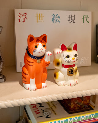 Orange ceramic fortune cat figurine with blue collar and gold bell on display