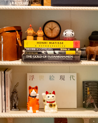 Orange ceramic fortune cat figurine on shelf, blue collar and gold bell visible