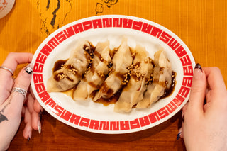 White oval gyoza plate with red patterned rim filled with cooked gyoza