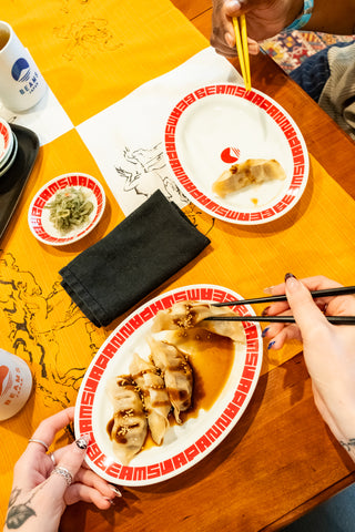 White oval gyoza plate with red patterned rim, holding cooked gyoza dumplings