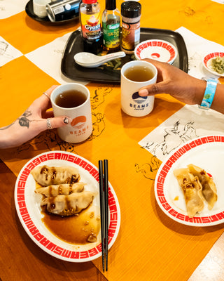 White sushi cup with BEAMS Japan logo, held at a table.
