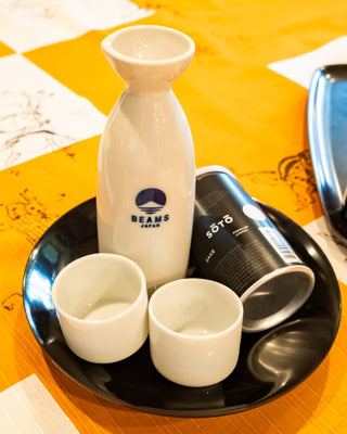 White ceramic sake bottle and two cups set with BEAMS Japan logo on tray