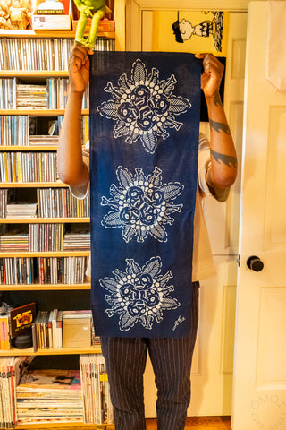 Navy blue tenugui towel held up indoors, showing white creature floral motifs