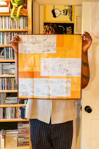 Orange and white handkerchief with gray animal line drawings, held up with brown border.