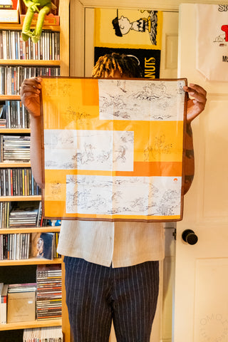 Orange and white handkerchief with gray animal sketches, held out with brown edge visible.