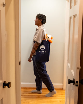 Navy BEAMS Japan tote bag with orange-and-white plush panda, carried by person