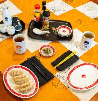 Table setting with dumplings, tea, and condiments on an orange checkered cloth