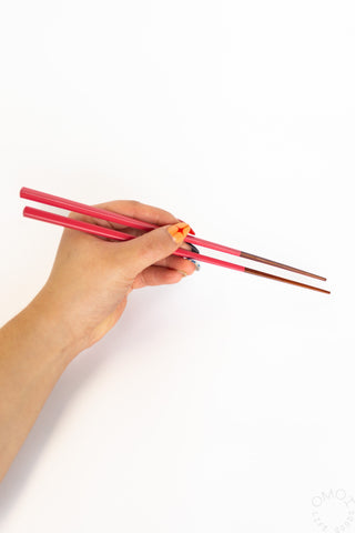 Red bamboo chopsticks with dark brown tips held in a hand, set of two.