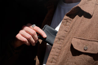 Bellroy black card slip held in hand near a coat, sleeve and card pocket visible