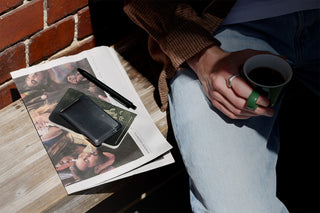 Bellroy black leather card slip on a table next to magazines and a coffee cup