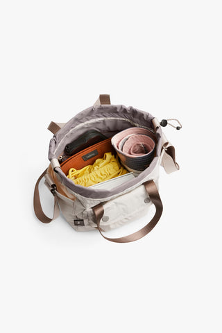 Oat cinch bucket bag open at top with drawstring; interior pockets and contents visible