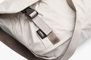 Oat light-beige messenger bag close-up of woven strap label and stitched seams
