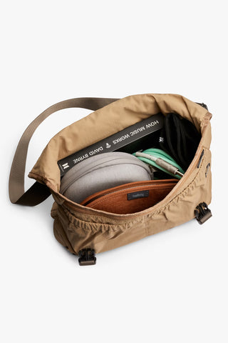 Sand-beige cinch messenger bag open, holding a water bottle and small card pouch