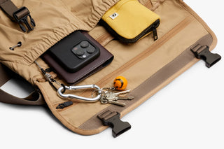 Sand-beige messenger bag with interior compartments holding keyring and small tech accessories
