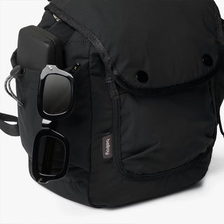Black mini backpack side view with clip hardware, external pocket, and adjustable shoulder strap