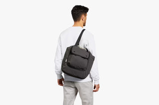 Dark crossbody tote bag worn on back with adjustable strap and zip pocket.