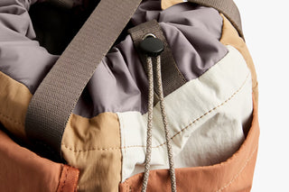 Cinch-top tan tote close-up with drawstring cords and gray webbing strap