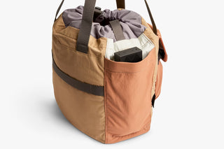 Tan cinch tote side view with dark-trim pocket and adjustable shoulder strap